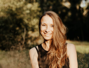 Elena, Spiritual Life Coach und Yogalehrerin, sitzt ruhig und lächelnd vor einem hellen Hintergrund. Sie steht für Achtsamkeit, Selbstliebe und ganzheitliche Begleitung mit Yoga, Meditation und Coaching.
